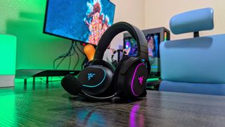 Two Razer Barracuda X Chroma headsets leaning against each other on a desk with a green backlight.